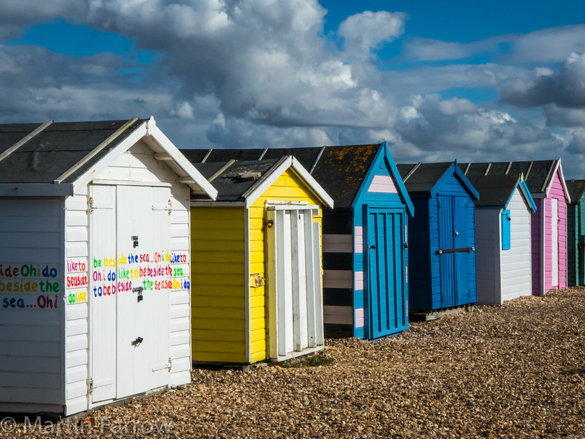 Oh-I-Do-Like-To-Be-Beside-The-Seaside 
 Beach huts on the shore 
 Keywords: Beach huts, Hayling Island, Solent, beach, blue, bright, closed, clouds, colour, ocean, pink, sand, sea, shingle, shore, water, yellow